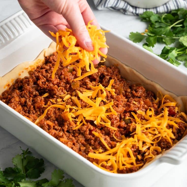 Process shot showing how to add the grated cheese on top of a crescent roll taco casserole.