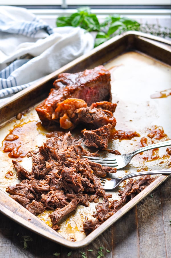Image shows the process of shredding a tender, slow cooked chuck roast with two forks. 