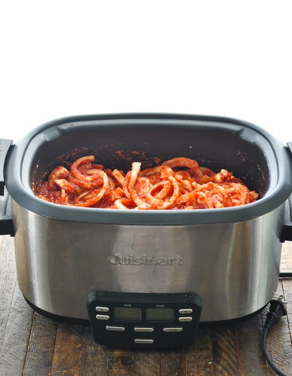 Sliced onions mixed into a tomato sauce in a large Cuisinart slow cooker.
