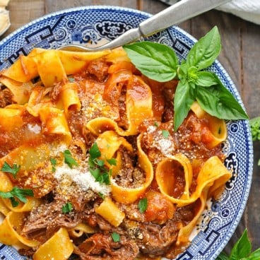 Close overhead shot of slow cooker beef ragu recipe served over pasta in a blue and white bowl