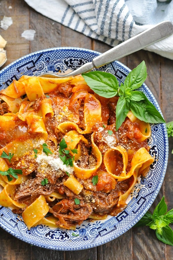 Close overhead shot of slow cooker beef ragu recipe served over pappardelle pasta in a blue and white bowl
