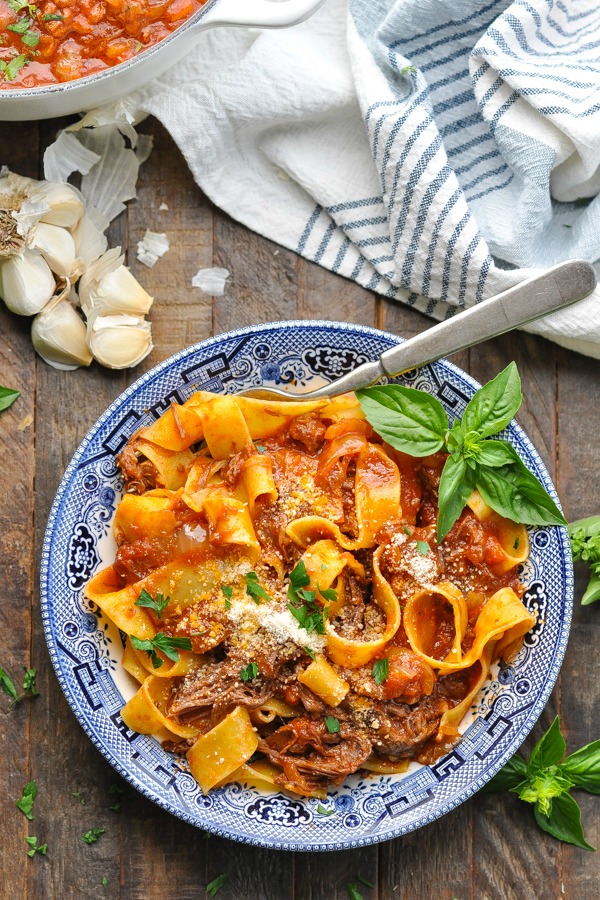 Long overhead shot of a bowl of beef ragu with pappardelle pasta and fresh basil