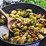 Wooden spoon in a skillet full of brussels sprouts with bacon and maple syrup