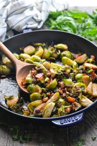 Wooden spoon in a skillet full of brussels sprouts with bacon and maple syrup