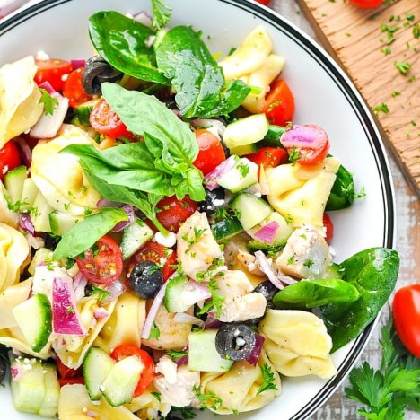 Overhead shot of a bowl of chicken and tortellini salad with fresh vegetables and herbs