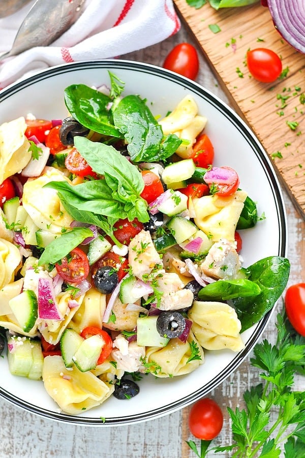 Overhead shot of a bowl of chicken and tortellini salad with fresh vegetables and herbs