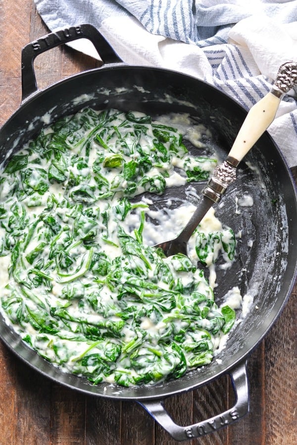 Overhead shot of easy creamed spinach recipe in a cast iron skillet with serving spoon