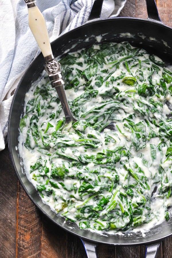 Overhead shot of creamed spinach recipe in a cast iron skillet on a wooden surface