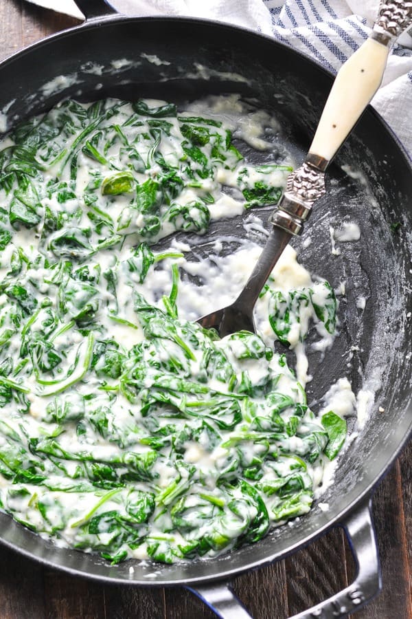 Close overhead shot of creamed spinach in a skillet with serving spoon