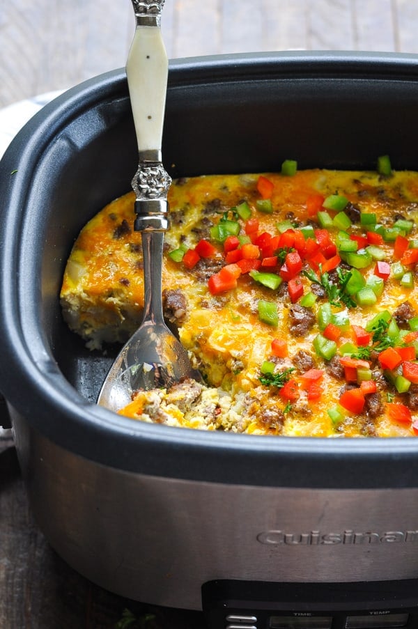 Spoon serving Crock Pot breakfast casserole topped with chopped fresh veggies