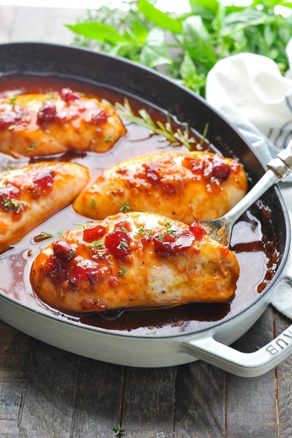 Close up front shot of cranberry orange chicken on a serving spoon in a casserole dish