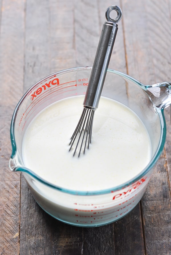 Cream and broth with a whisk in a glass mixing bowl