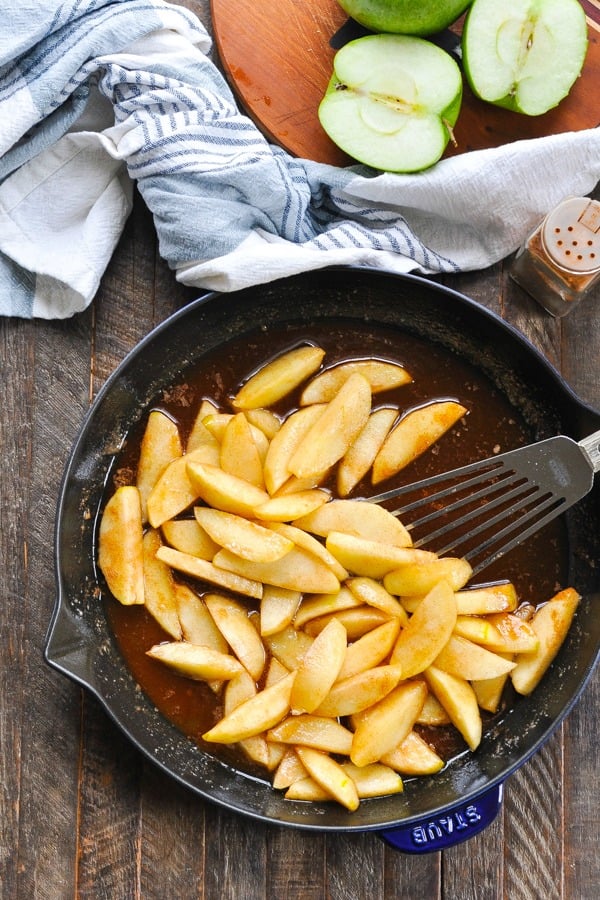 Overhead shot of cast iron skillet full of fried apples on a wooden surface