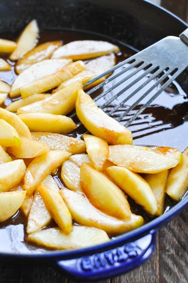 Close up shot of spatula with fried cinnamon apples in a skillet