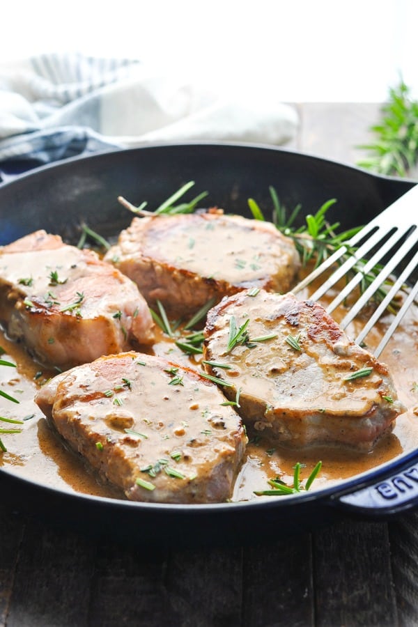 Front shot of boneless stovetop pork chops in a cast iron skillet with cider gravy