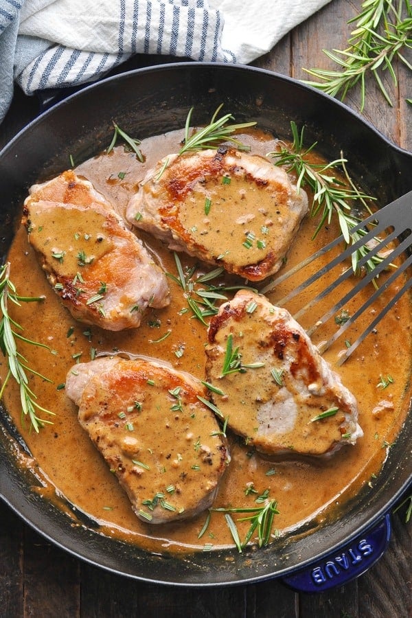 Close up shot of four boneless stove top pork chops in a skillet with apple cider gravy