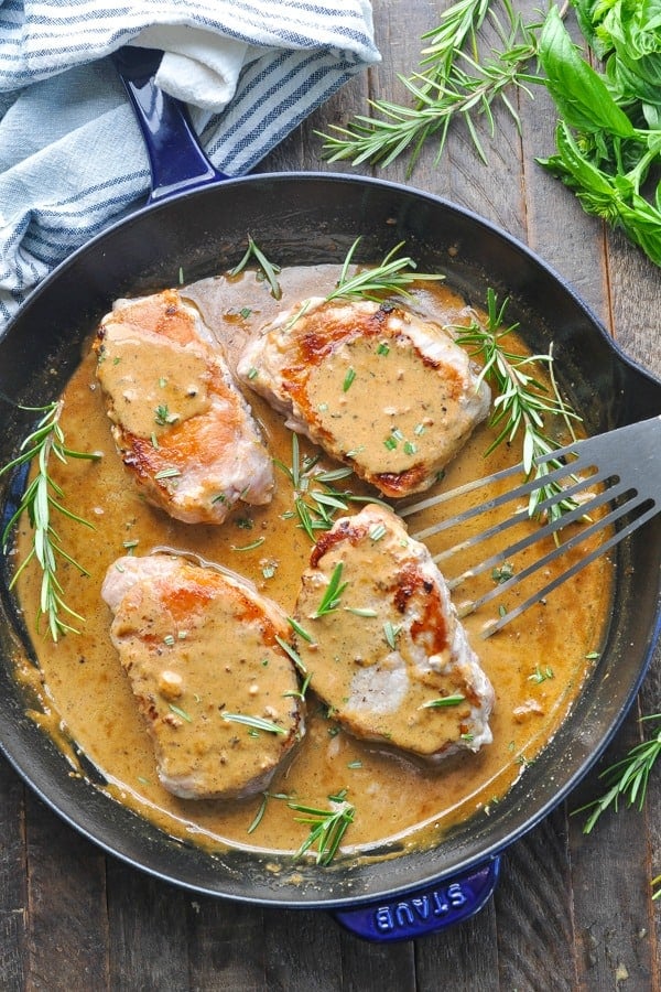 Overhead shot of four pan fried pork chops in gravy in a cast iron skillet