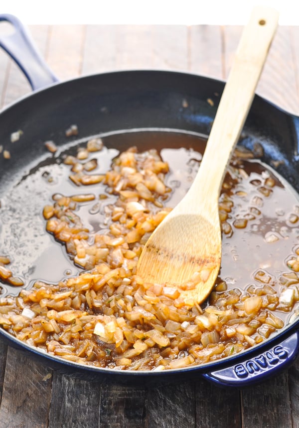 Sauteed onions in a cast iron skillet with wooden spoon