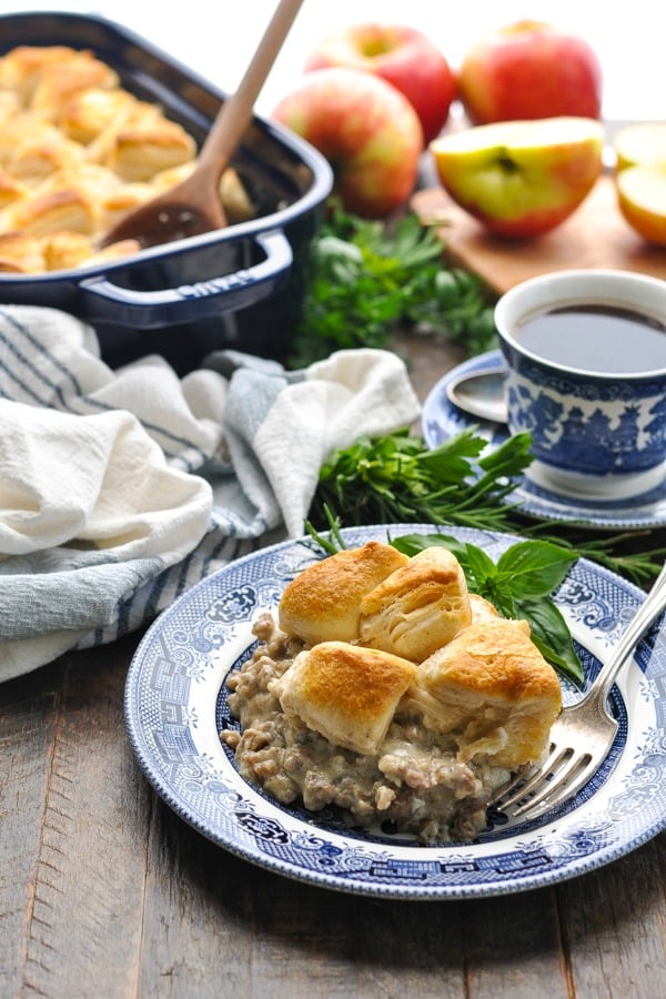 Front shot of biscuits and gravy casserole on a wooden surface with fresh herbs and a cup of coffee