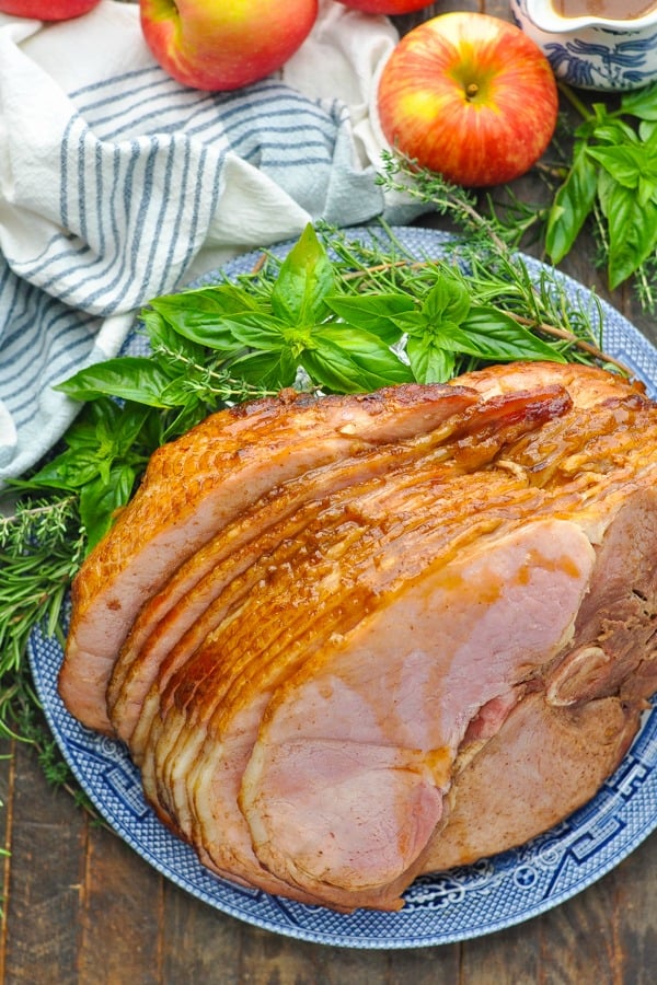 Overhead shot of Crock Pot Ham with Cola Glaze on a platter surrounded by herbs