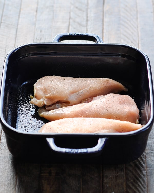 Raw boneless skinless chicken breasts in a blue baking dish