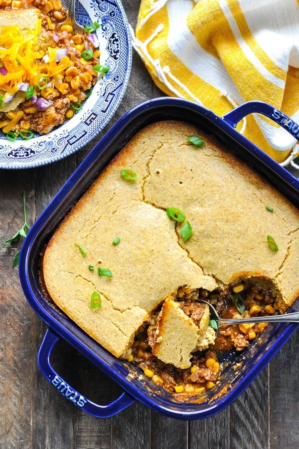 Overhead shot of ground beef casserole with cornbread in a blue dish on a wooden surface