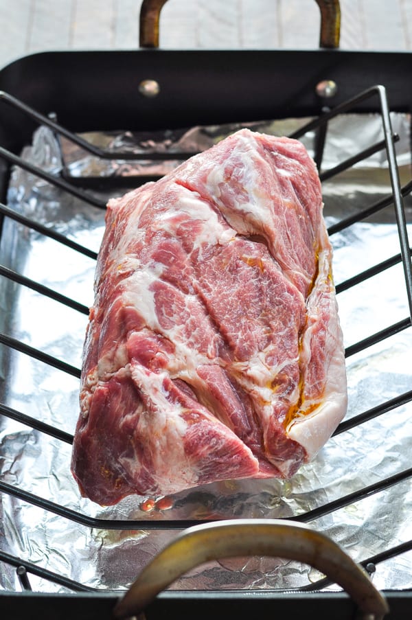 Raw pork shoulder in a roasting pan on a rack