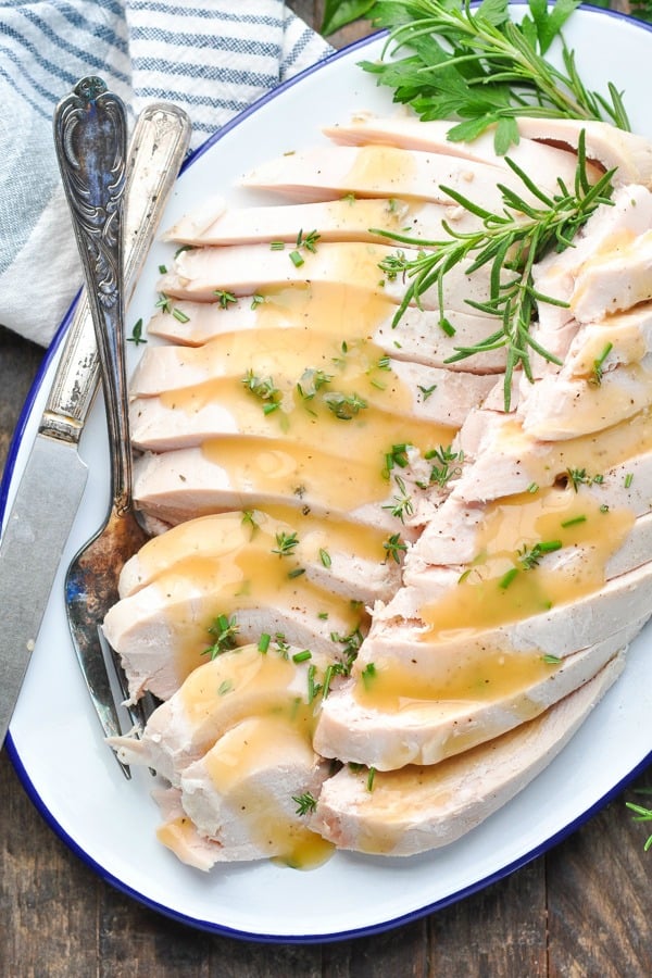 Overhead shot of sliced turkey breast on a serving tray garnished with fresh herbs