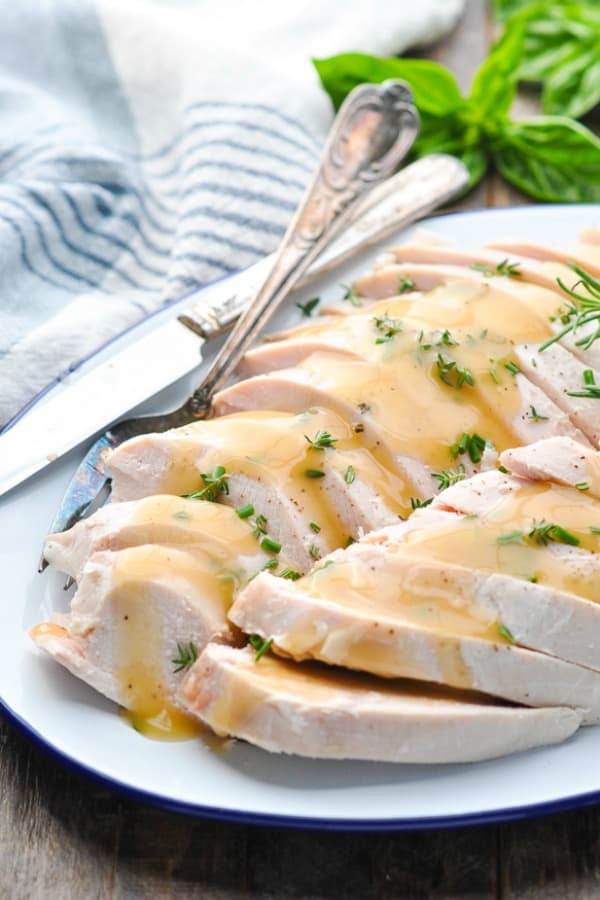 Sliced slow cooker turkey breast on a white serving tray with gravy on top
