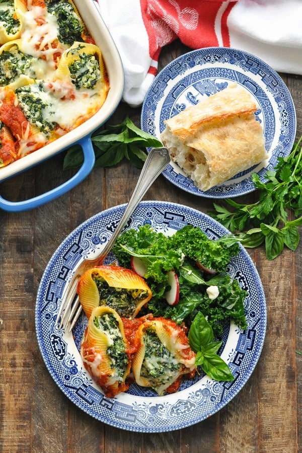 Overhead shot of spinach stuffed shells on a plate with salad and a side of baguette