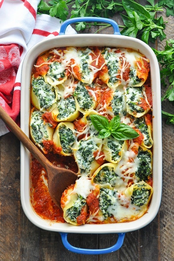 Long overhead shot of baked Spinach Stuffed Shells in a baking dish with wooden spoon