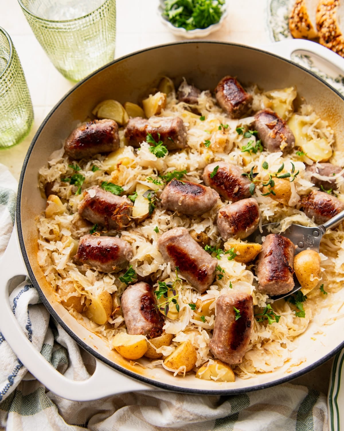 Close up side shot of a cast iron pan full of bratwurst and sauerkraut and potatoes.