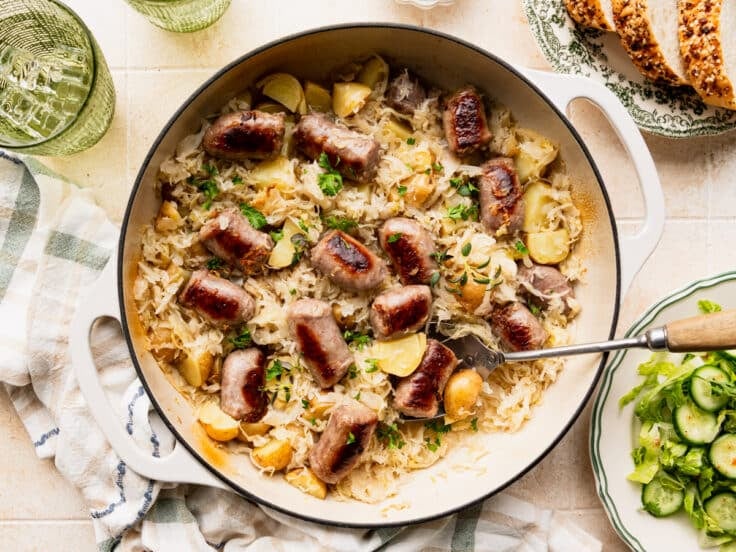 Horizontal overhead shot of a pan of bratwurst with sauerkraut and potatoes.