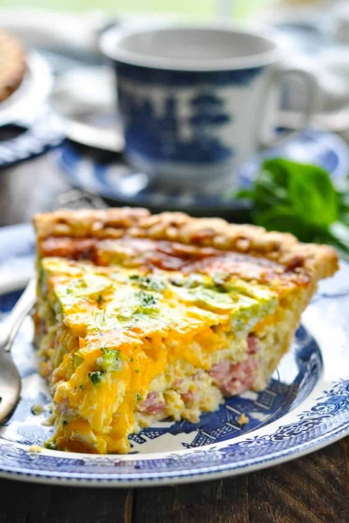 Close up front shot of a cheesy slice of ham and broccoli quiche on a plate.