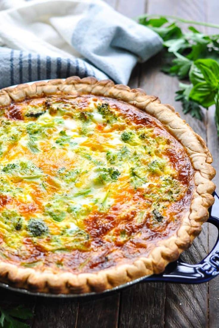Baked ham, cheese, and broccoli quiche in a blue pie plate on a wooden table.