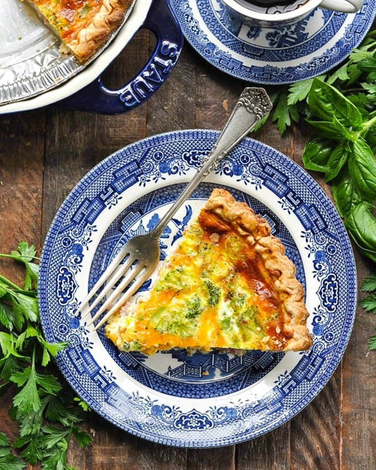 Overhead image of the best ham and broccoli quiche on a plate with a mug of coffee on the side.