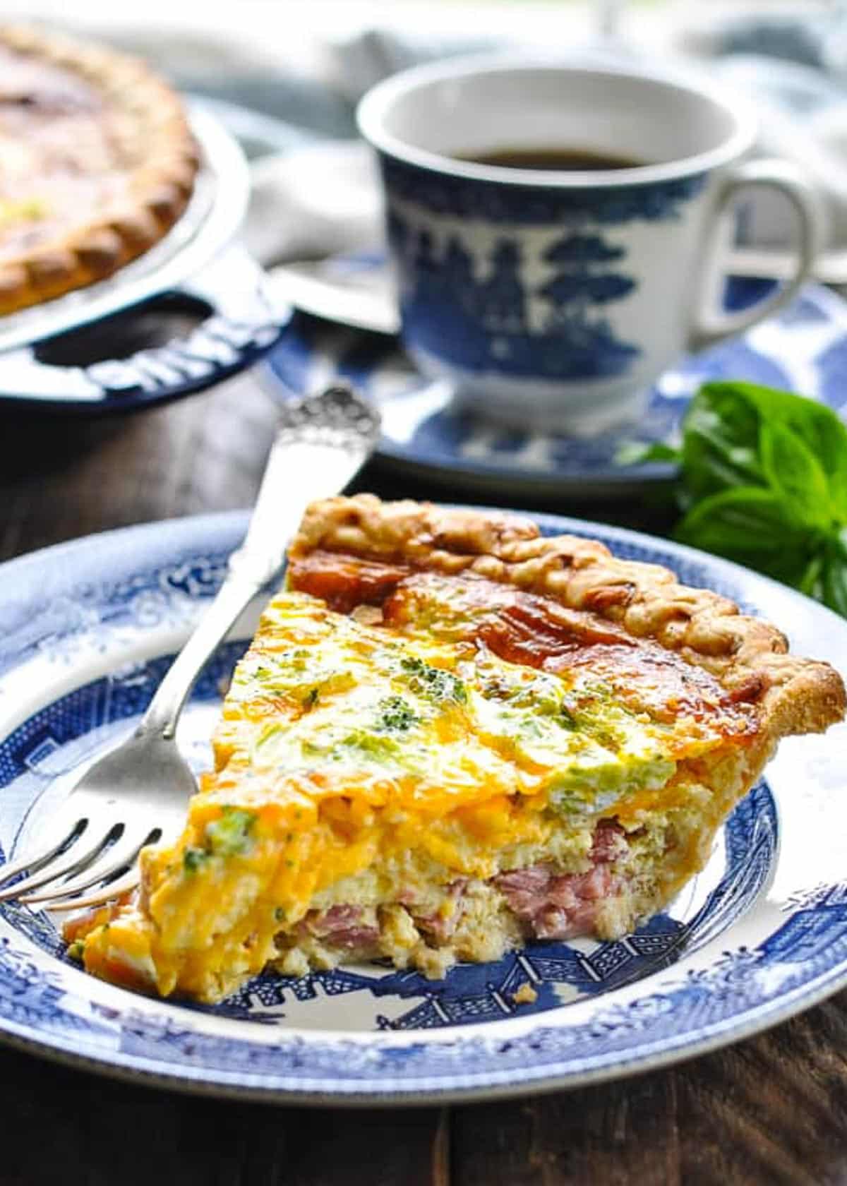 Side shot of a slice of quiche with broccoli and ham on a blue and white plate.