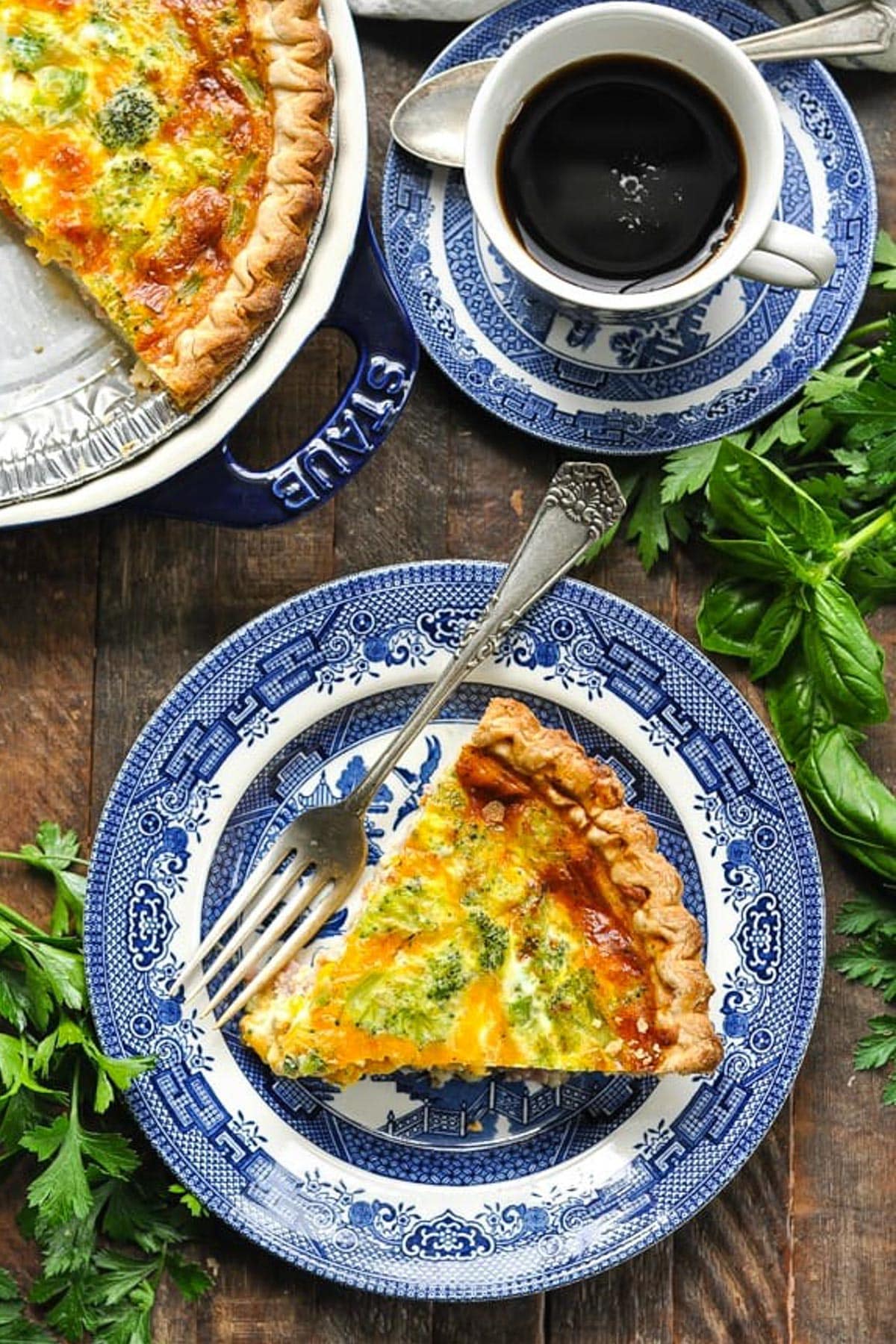 Overhead shot of a plate of ham and broccoli quiche on a wooden table with a cup of coffee.