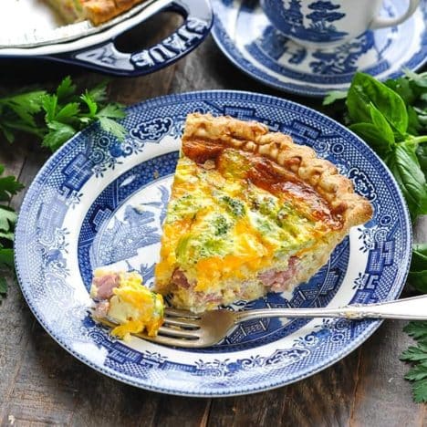 Square side shot of a slice of easy ham and broccoli quiche on a blue and white plate.