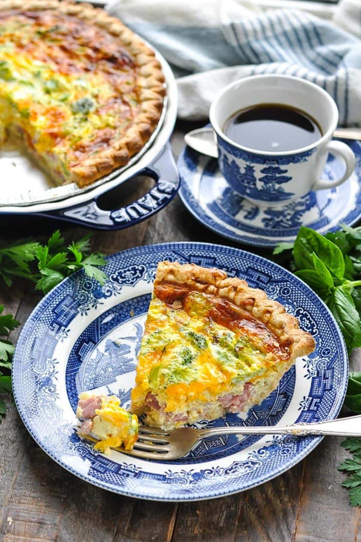 Table with a ham and broccoli quiche and fresh herbs.