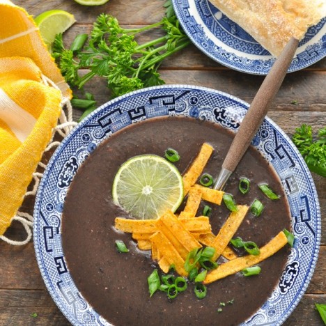 Close overhead shot of a bowl of healthy black bean soup recipe topped with tortilla strips and green onions and lime.