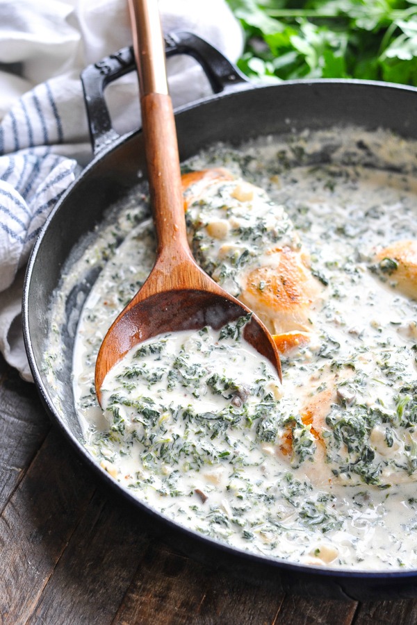 Wooden spoon scooping up chicken florentine sauce from a skillet
