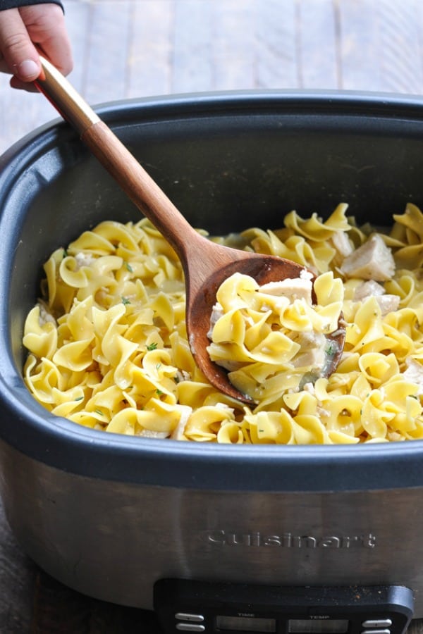 Wooden spoon scooping up chicken and noodles from a slow cooker
