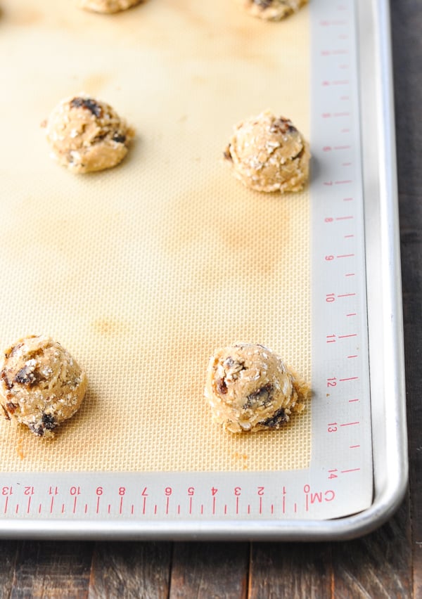 Rows of oatmeal raisin cookie dough lined up on a silicone baking sheet-lined cookie tray.