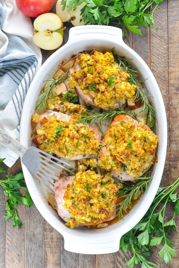 Overhead shot of pork chops with stuffing surrounded by fresh herbs in a white dish
