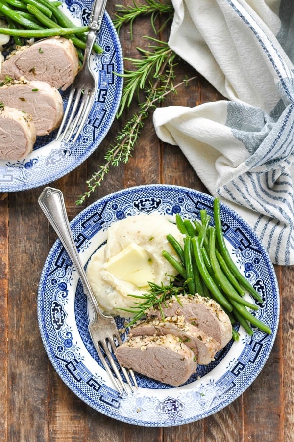 Overhead shot of pork tenderloin slices on a plate with green beans and mashed potatoes