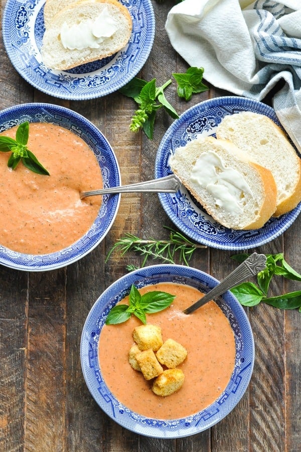 Two bowls of Cream of Tomato Soup on a wooden table with French bread on the side