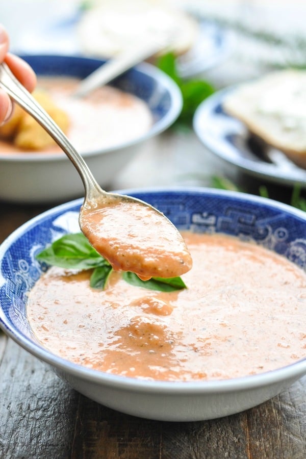 Close up shot of a spoon scooping up tomato bisque from a blue and white bowl