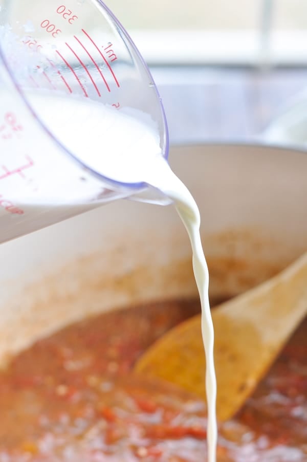 Pouring heavy cream into a pot for tomato bisque soup