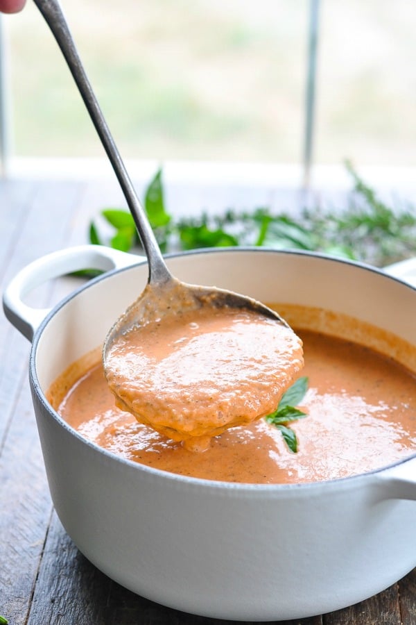 Ladle scooping up smooth and creamy tomato bisque soup from a white pot